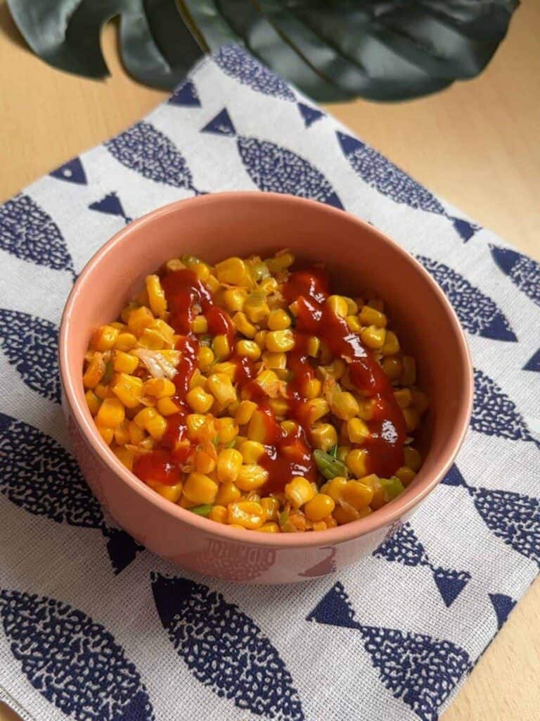 Close-up photo of a plate of sizzling Bap xao, a popular Vietnamese stir-fried corn dish. The dish features golden kernels of corn sautéed with dried shrimps and scallions