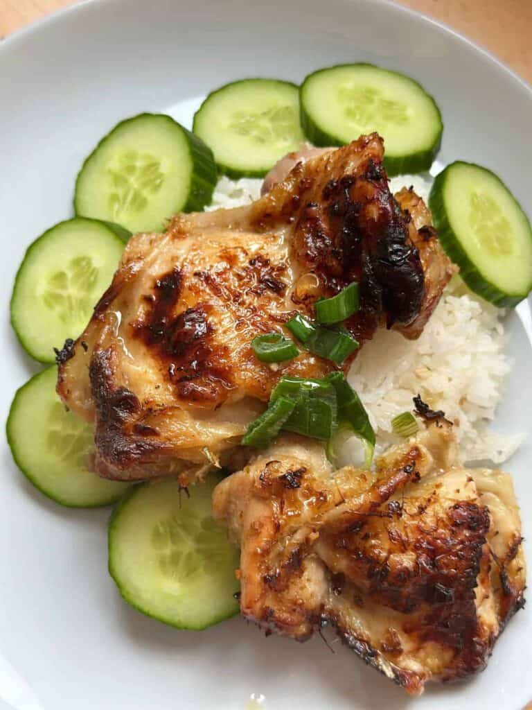 An image of Air Fryer Vietnamese Lemongrass Chicken served on a plate. The chicken is marinated in a blend of lemongrass, garlic, scallions, and other spices. It is garnished with green onion oil and herbs and served with rice.