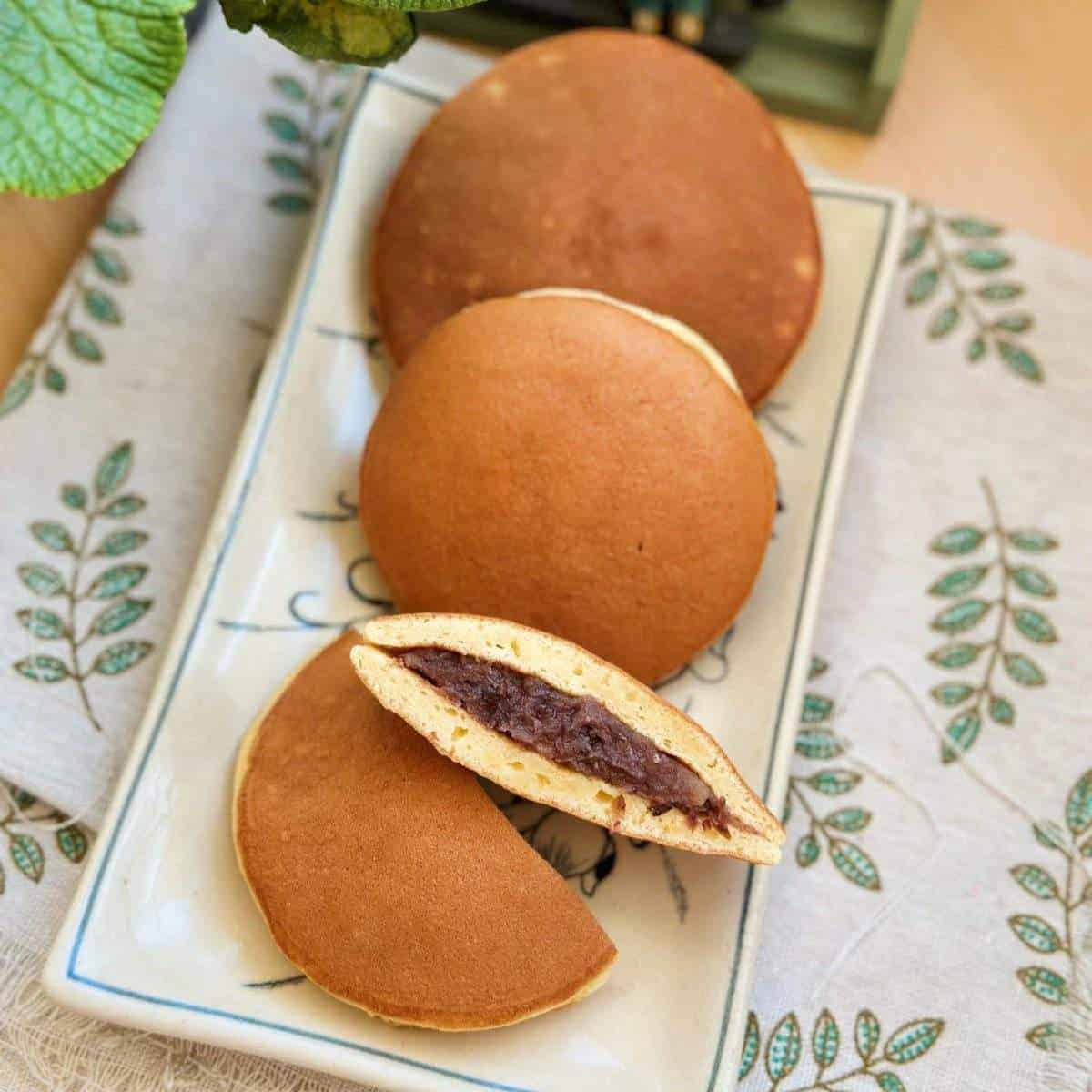 Three pairs of Dora Cakes, sweet red bean paste sandwiched between two fluffy pancakes, arranged neatly on a rectangular dish.