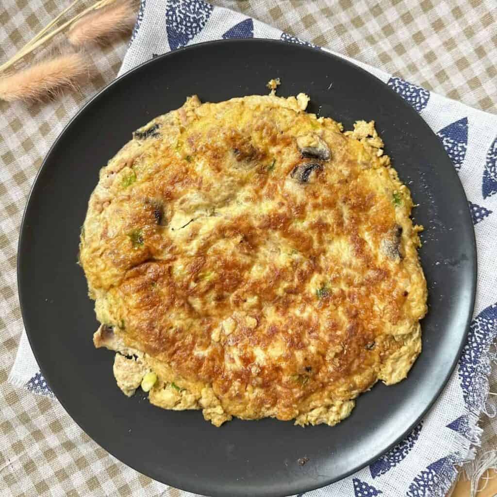 Enoki Beef Rolls Over Rice (Super Easy) "Image of a Vietnamese-style omelette on a plate, with a golden brown exterior and a fluffy, yellow interior."