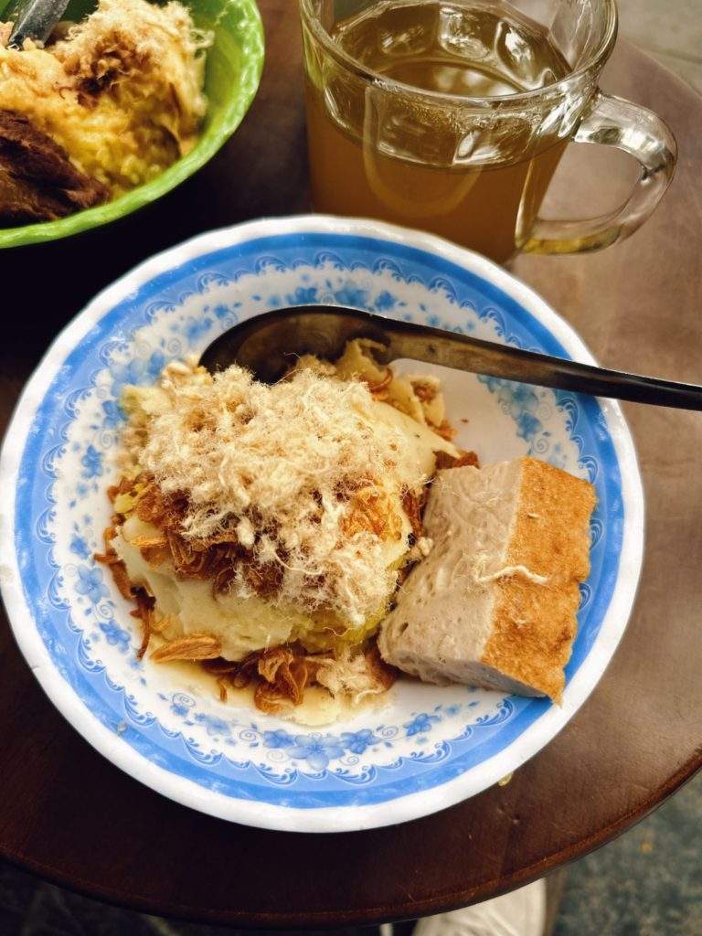 A tempting photo of Xoi Xeo, featuring yellow sticky rice with steamed mung bean paste, crispy fried shallots, pork floss, and cha que (Vietnamese cinnamon pork sausage).