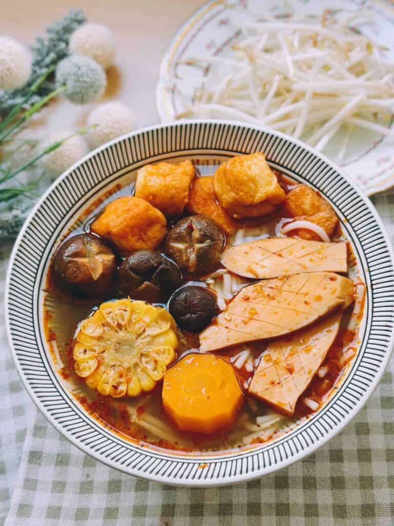 Vibrant and flavorful Bun Bo Hue Chay (Vegan Bun Bo Hue) soup, featuring a rich broth filled with noodles, tofu, vegetables, and aromatic herbs, topped with fresh lime wedges and chili peppers for a tantalizing and satisfying dining experience