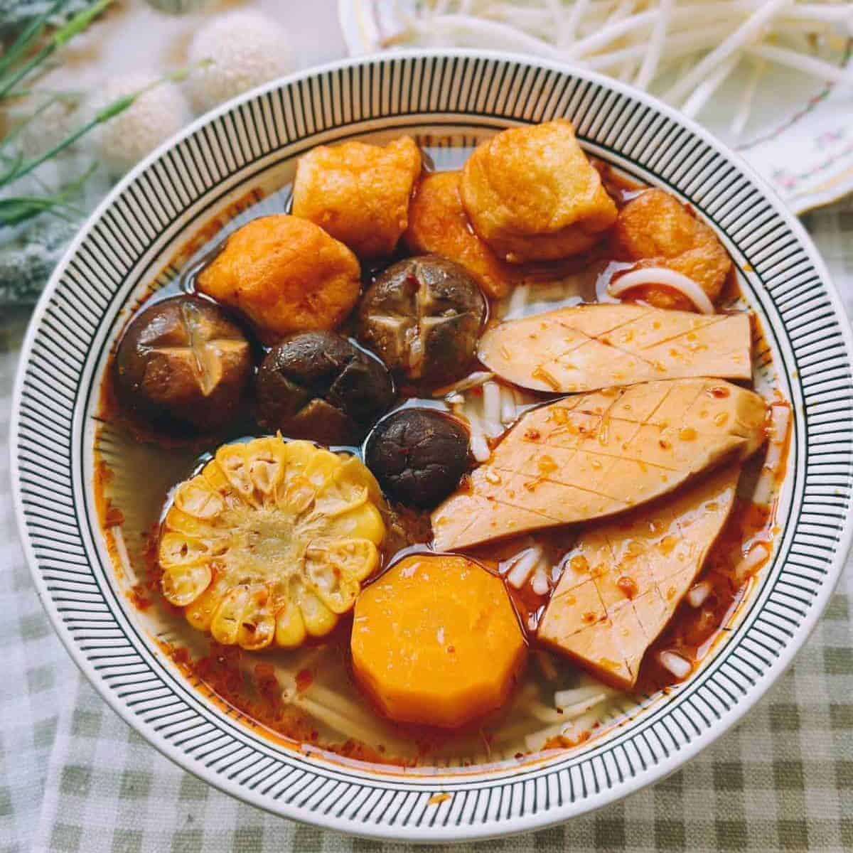 Vibrant and flavorful Bun Bo Hue Chay (Vegan Bun Bo Hue) soup, featuring a rich broth filled with noodles, tofu, vegetables, and aromatic herbs, topped with fresh lime wedges and chili peppers for a tantalizing and satisfying dining experience