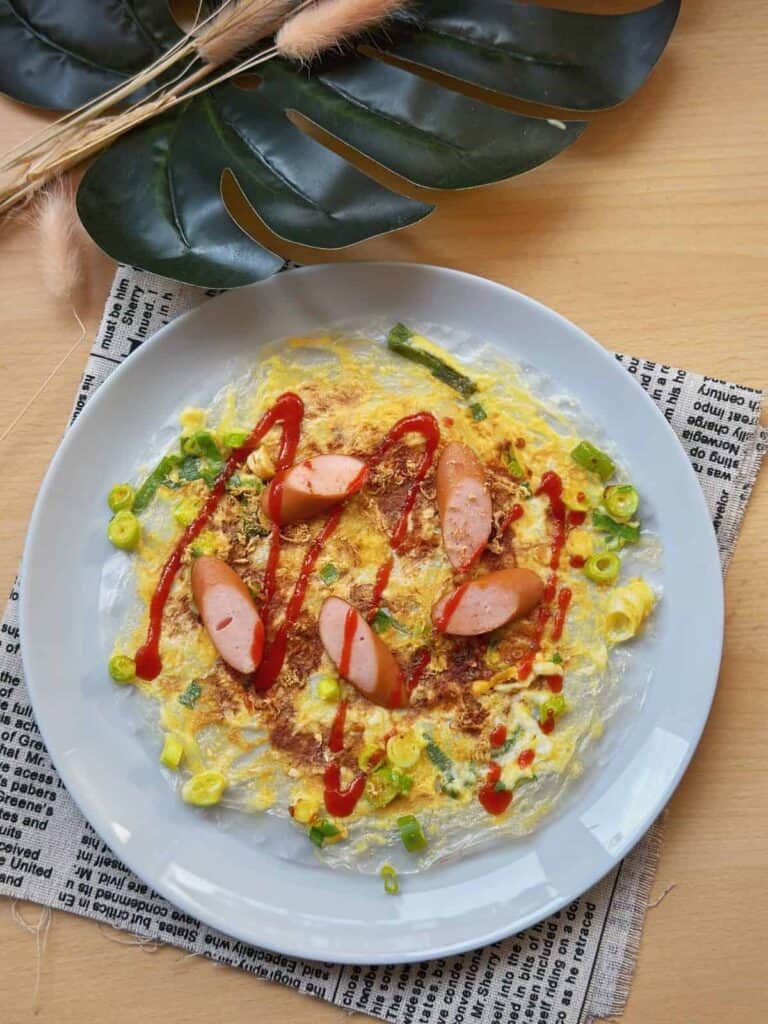 A mouthwatering plate of Bánh Tráng Nướng, Vietnamese Pizza, with a crispy golden-brown texture. Topped with a flavorful combination of eggs, scallions, and a variety of savory ingredients.