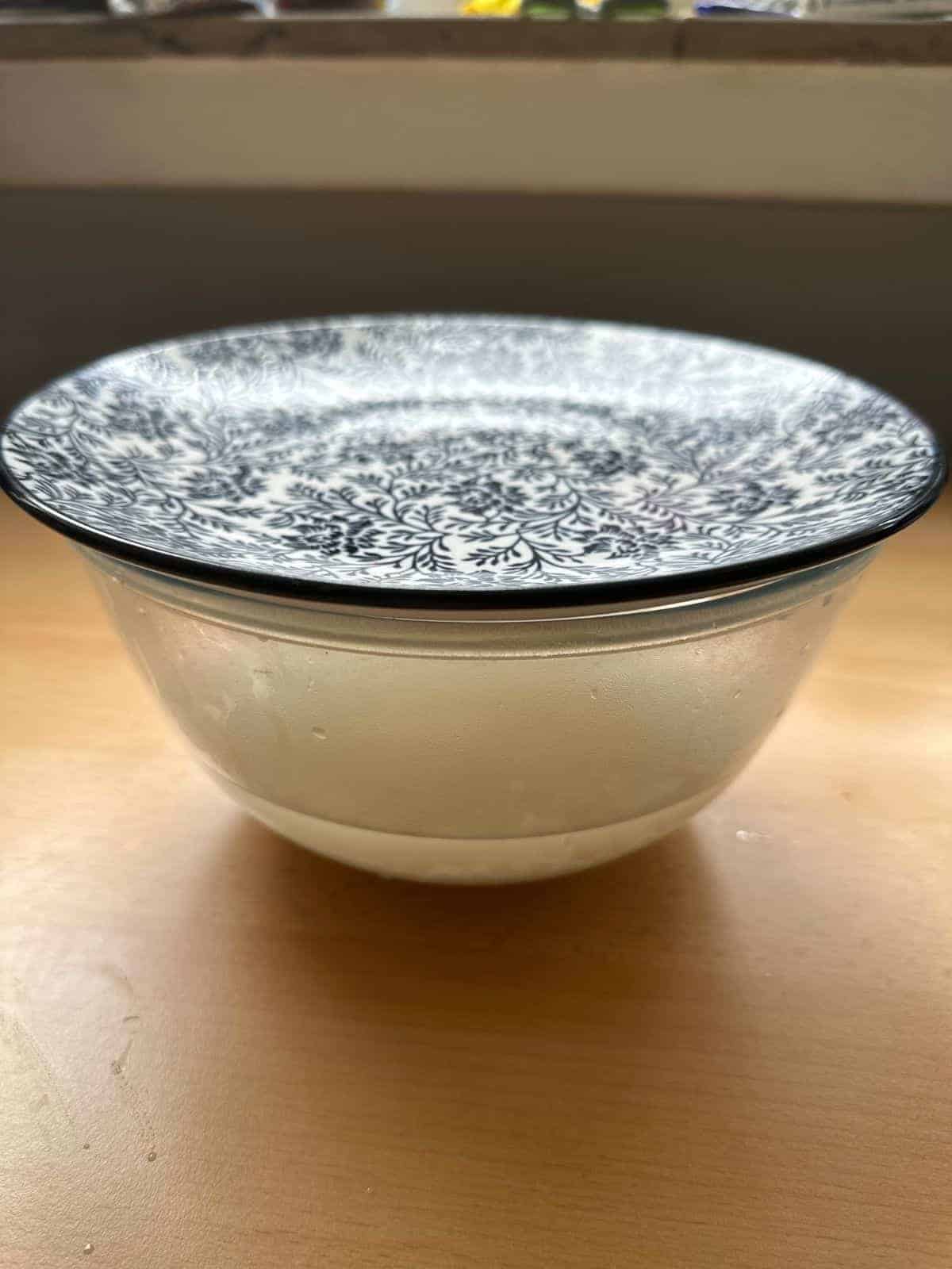 The Best Microwave Jasmine Rice (Asian-Approved) a bowl of rice soaked in water with a plate as lid