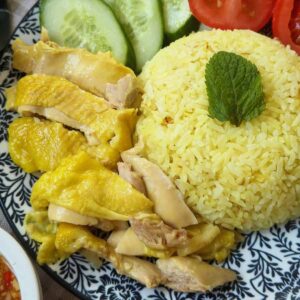 A delicious plate of Vietnamese Hainanese chicken rice with fragrant rice, tender chicken, and ginger fish sauce, garnished with herbs and served with cucumber and tomato slices