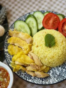 A delicious plate of Vietnamese Hainanese chicken rice with fragrant rice, tender chicken, and ginger fish sauce, garnished with herbs and served with cucumber and tomato slices