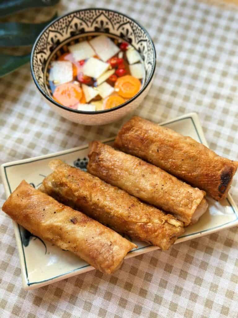 A platter of Hanoi spring rolls, showcasing their crispy golden exterior and flavorful filling, served with a side of dipping sauce