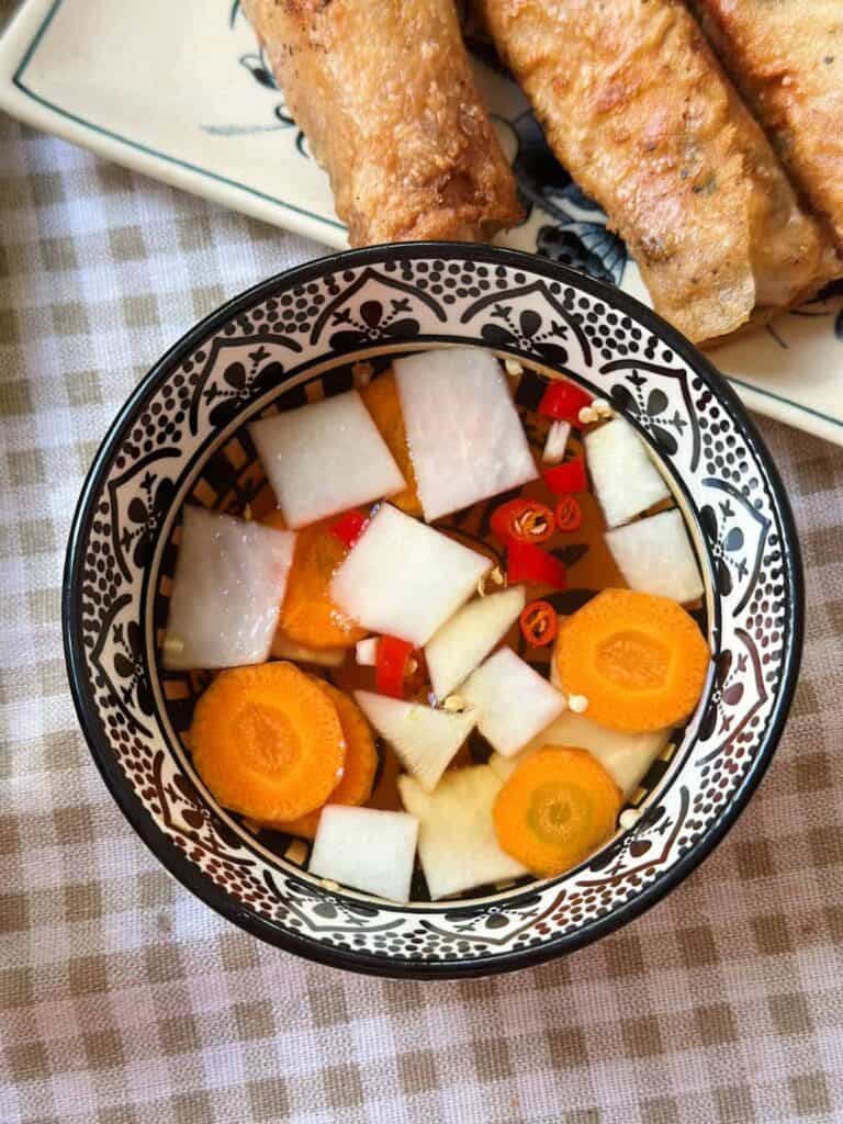 Close-up of a bowl filled with Hanoi-style dipping fish sauce, garnished with sliced carrots, kohlrabi.