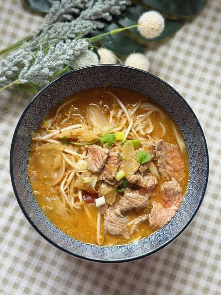 Steaming bowl of Pho Sa Tế with flat rice noodles, rich satay broth, and an assortment of fresh toppings