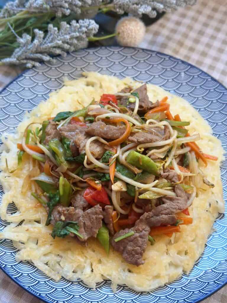 a plate of Pho Xao Gion, a Vietnamese dish featuring crispy fried Pho noodles topped with stir-fried beef and a medley of fresh herbs and vegetables
