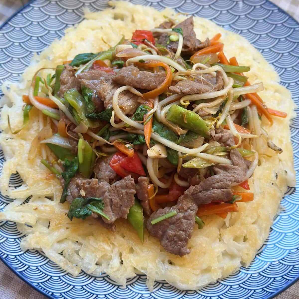 a plate of Pho Xao Gion, a Vietnamese dish featuring crispy fried Pho noodles topped with stir-fried beef and a medley of fresh herbs and vegetables