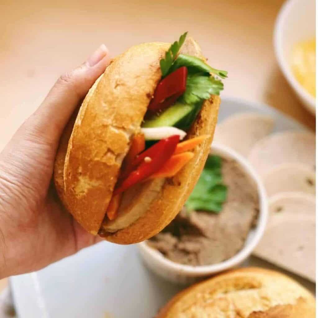 A close-up photo of a delicious Banh Mi sandwich with a crispy baguette, filled with vibrant vegetables, fresh herbs, and savory protein.