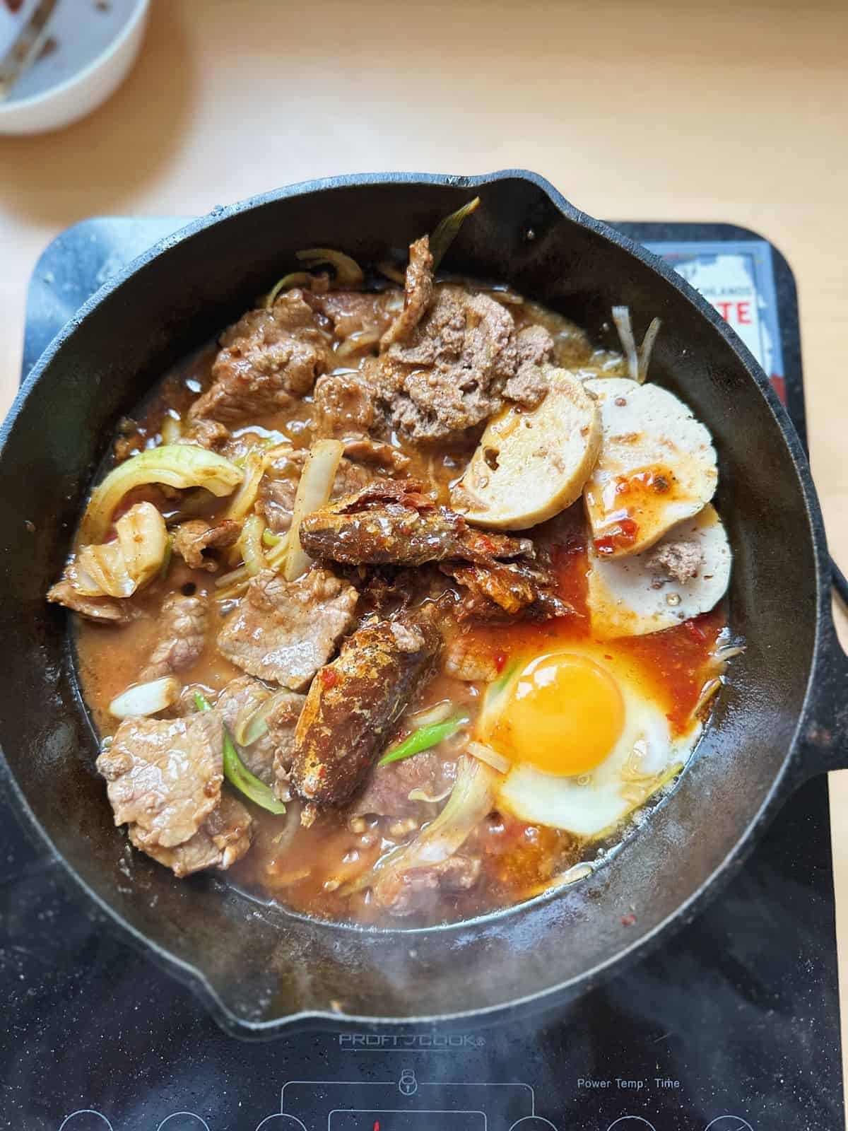 A pan of stir-fried beef, sunny-side-up eggs, canned fish, Vietnamese liver pâté and sausages.