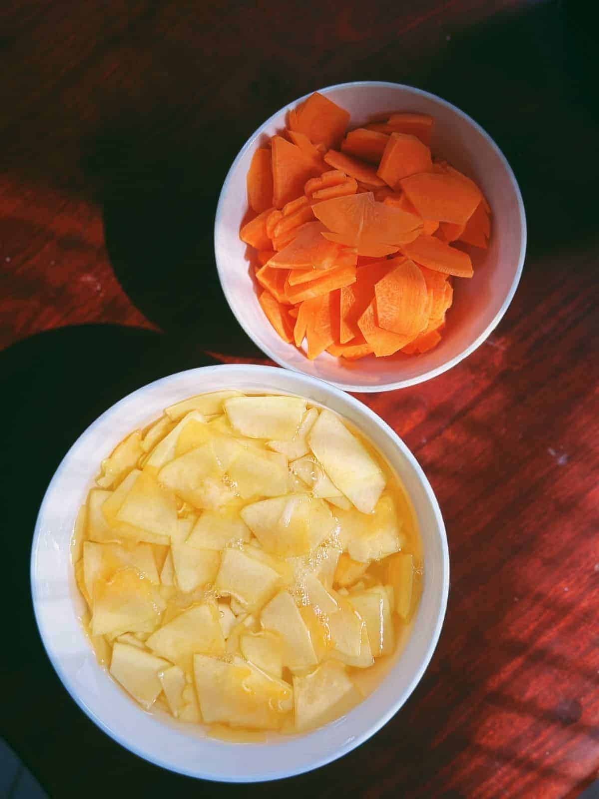 Original Bún Chả (gegrilltes Schweinefleisch aus Hanoi) Thin slices of green papaya in a bowl of salt water and thin slices of carrots in another bowl.