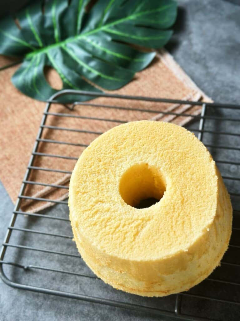 Top view of a whole Chinese chiffon cake with a center tube, resting on a wire rack over a rustic cloth and tropical leaf.