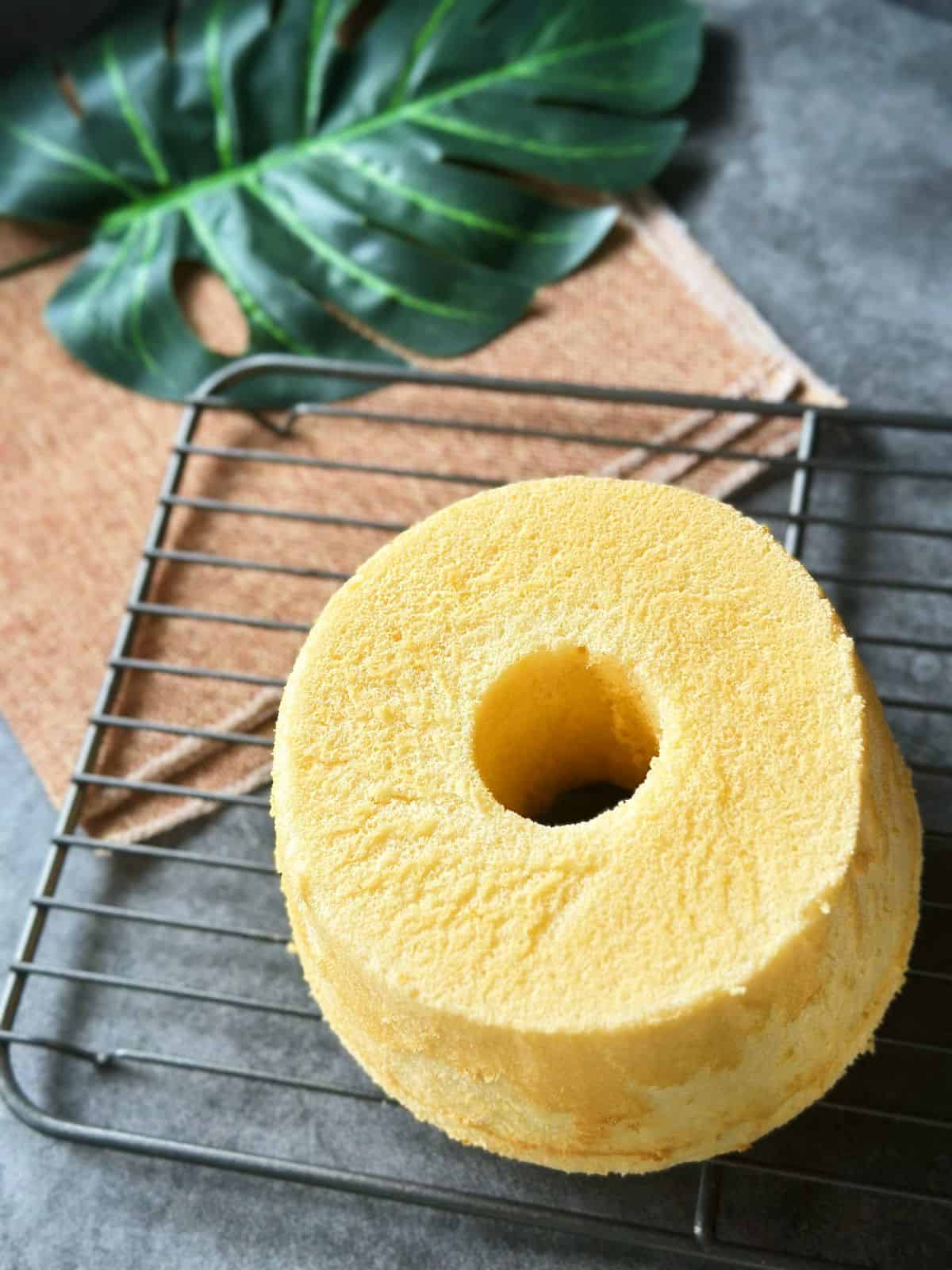 Fluffiger Chiffon Kuchen / Chiffon Cake / シフォンケーキ Top view of a whole Chinese chiffon cake with a center tube, resting on a wire rack over a rustic cloth and tropical leaf.
