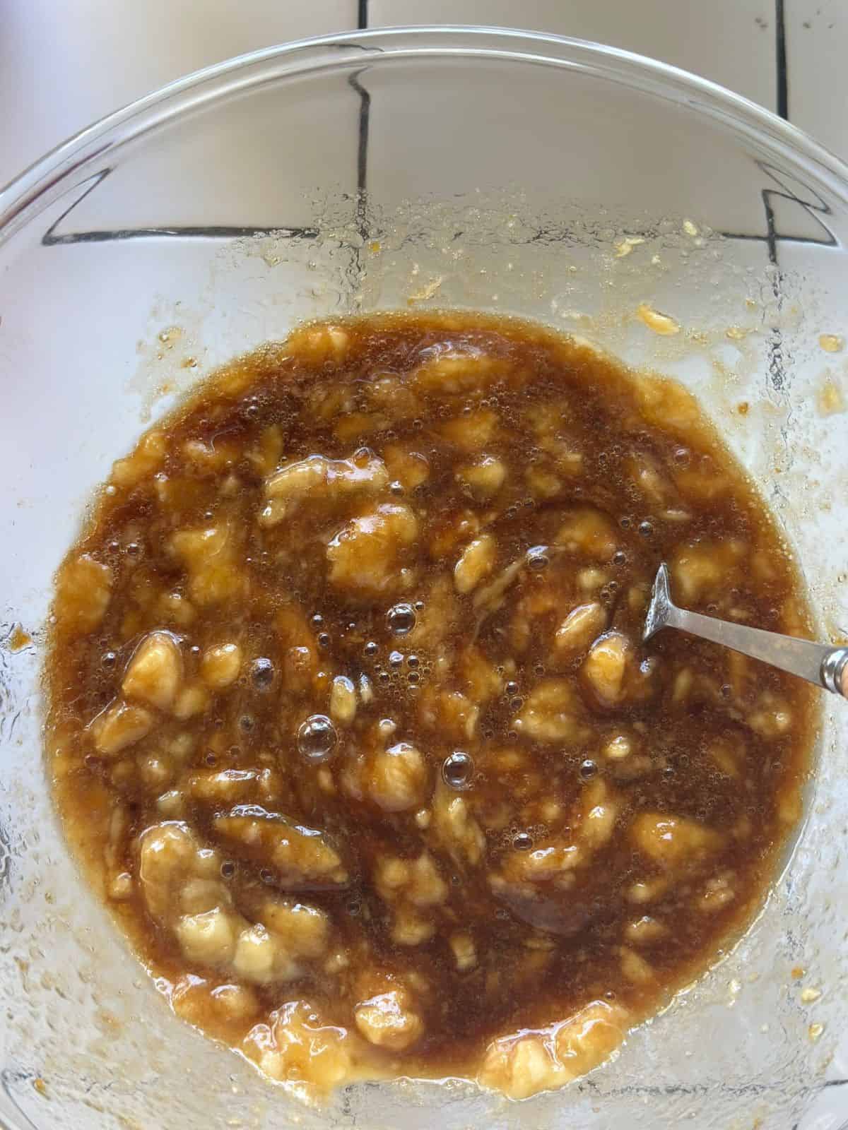 Eine Glasschüssel mit zerdrückten Bananen, Zucker und Öl, zu einer feuchten Masse verrührt, bereit für die Muffinzubereitung.