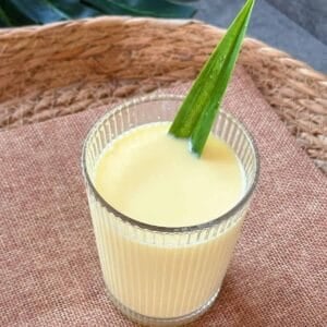 A glass of Vietnamese corn milk (Sữa Bắp) with a pandan leaf garnish, placed on a woven tray.