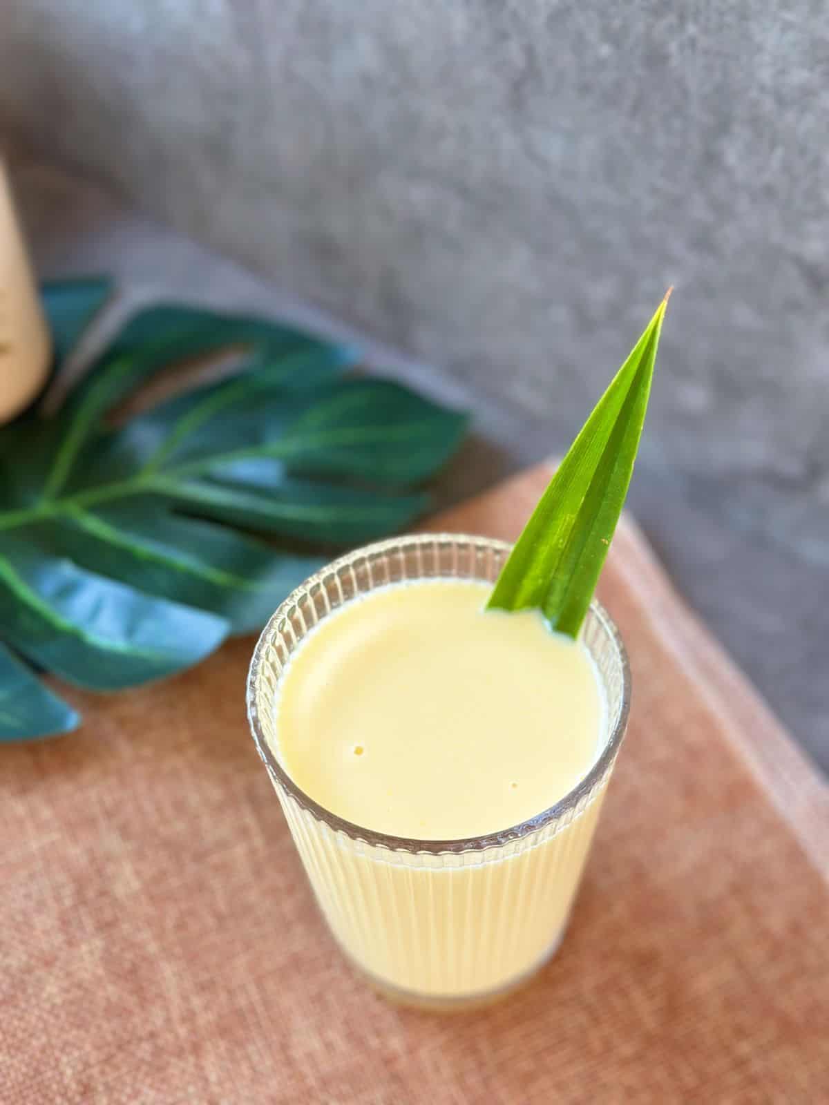 Corn Milk (Vietnamese Sữa Bắp) A glass of Vietnamese corn milk (Sữa Bắp) with a pandan leaf garnish, placed on a woven tray.