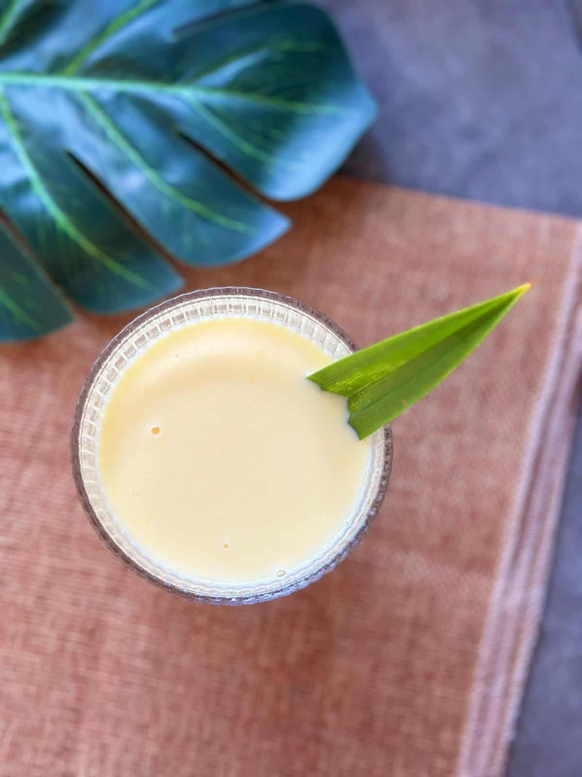 Corn Milk (Vietnamese Sữa Bắp) A glass of Vietnamese corn milk (Sữa Bắp) with a pandan leaf garnish, placed on a woven tray.