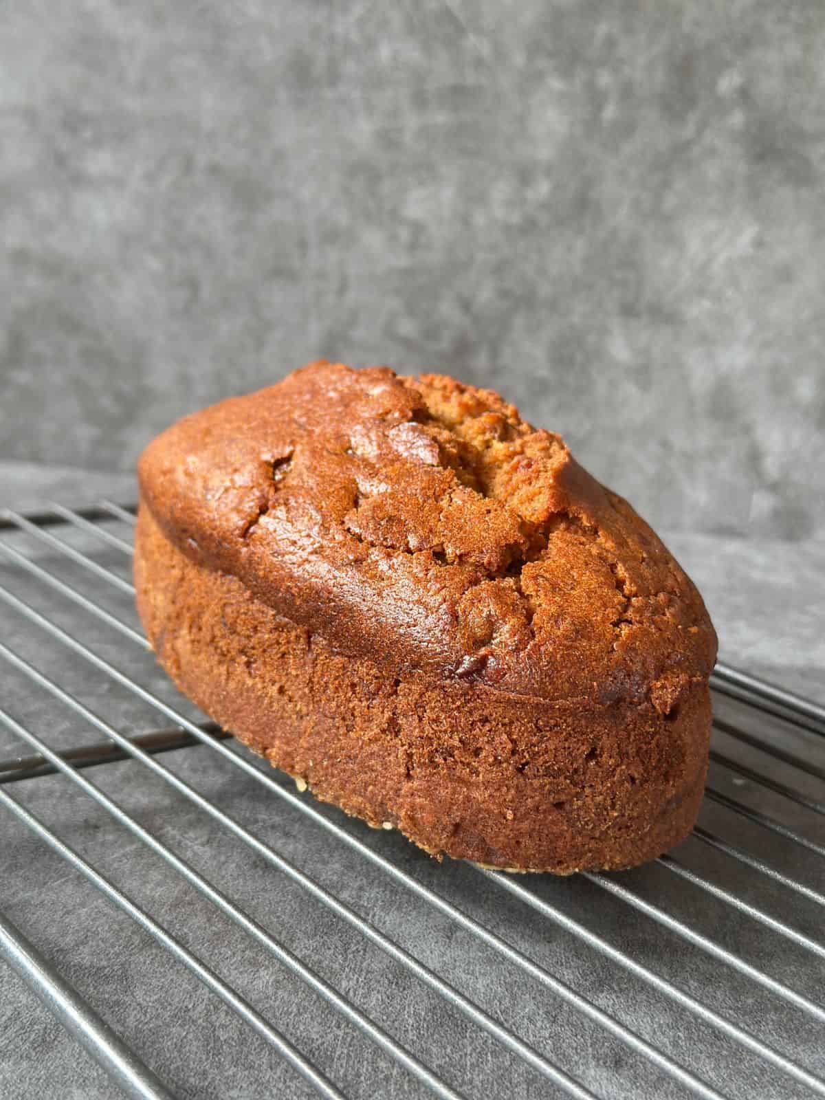 Bester Bananenkuchen – Saftig & Einfach Gelingsicher Seitliche Ansicht eines goldbraun gebackenen Bananenkuchens auf einem Kuchengitter vor grauem Hintergrund.