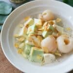 A bowl of Chè Khúc Bạch with white and green pudding cubes, lychees, basil seeds, and toasted almond slices in chilled syrup.