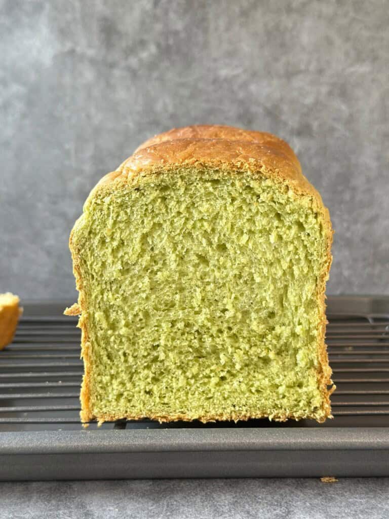 Close-up of a sliced pandan bread loaf showing its soft, fluffy green crumb and golden crust.