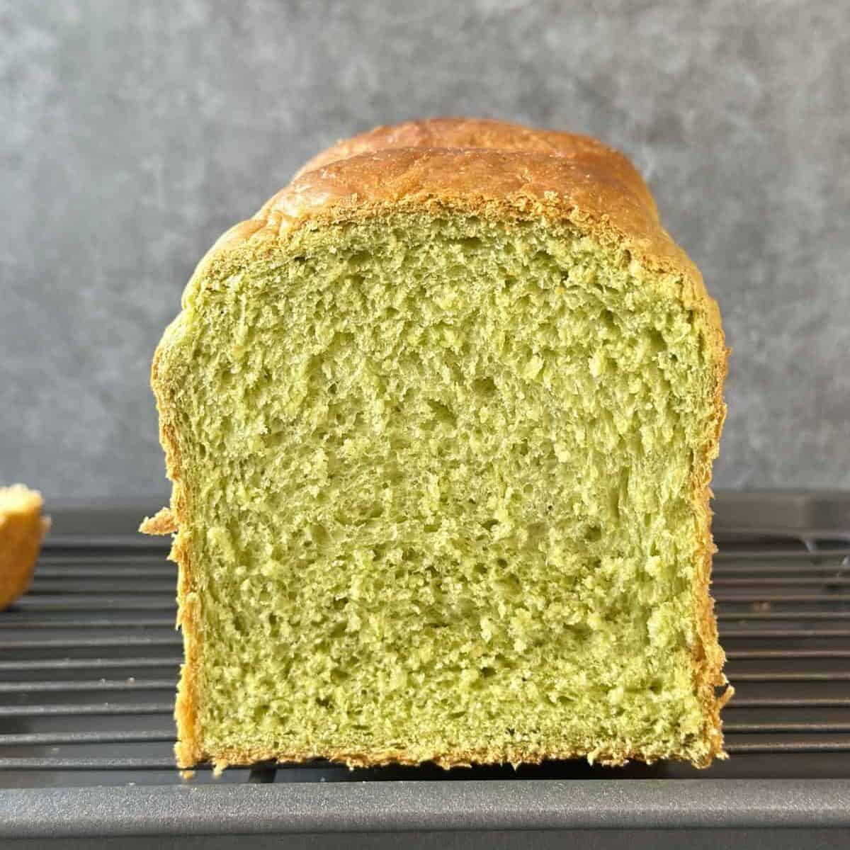 Close-up of a sliced pandan bread loaf showing its soft, fluffy green crumb and golden crust.