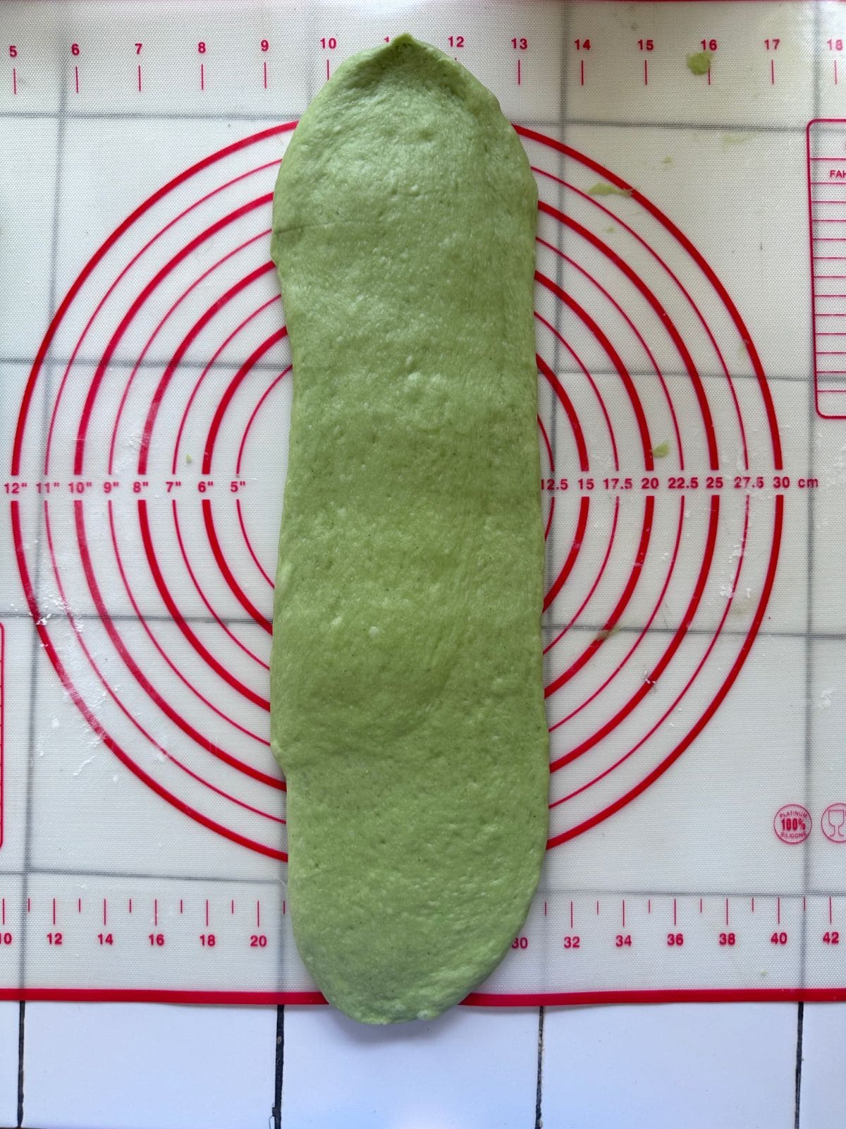 Pillow-Soft Pandan Bread (Vegan) Flattened green dough rolled out into a longer, more even oval shape on the baking mat.