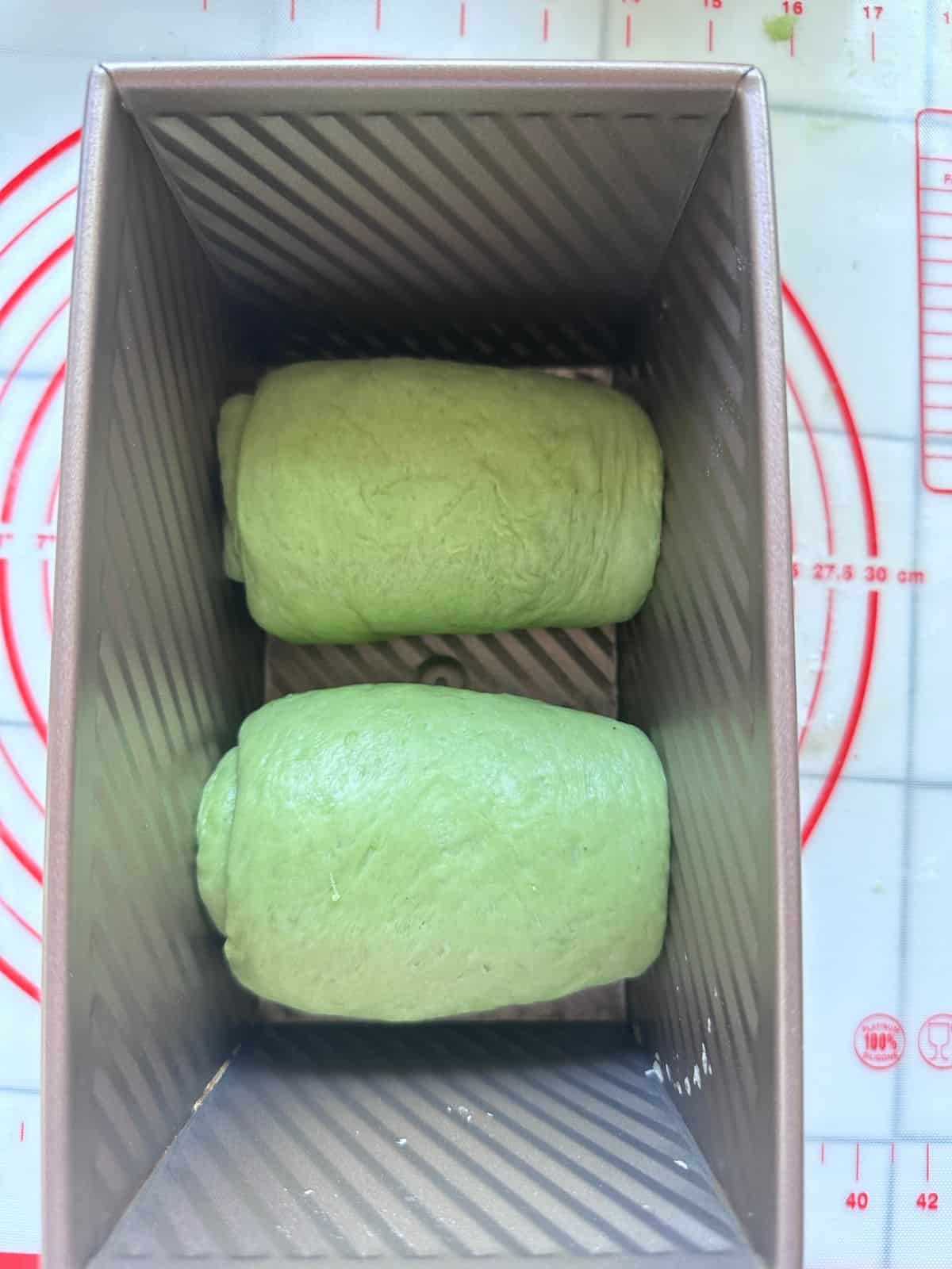 Pillow-Soft Pandan Bread (Vegan) Two smooth green dough logs placed side by side inside a rectangular bread loaf pan, ready for proofing or baking.