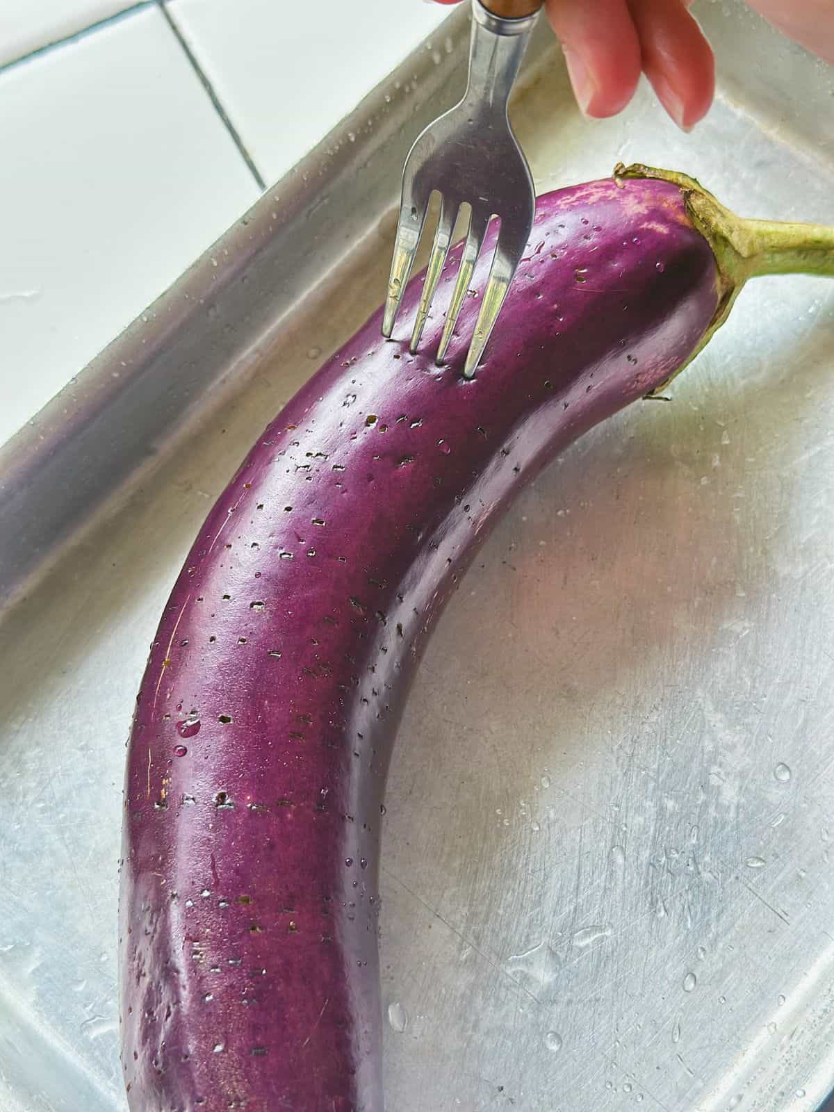 Fresh eggplant being poked with a fork before grilling.