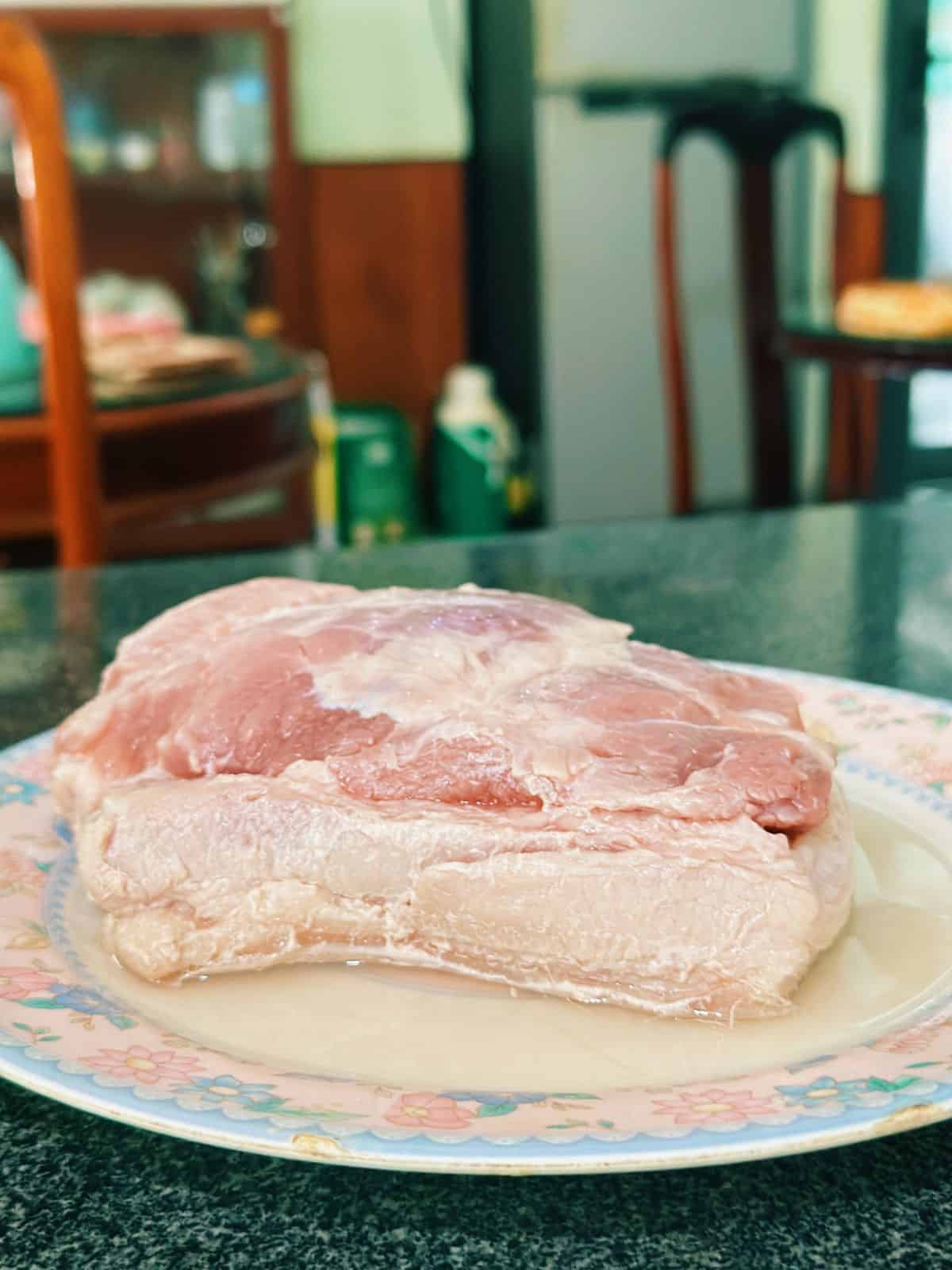 The blanched pork belly resting on a plate with the skin side soaking in white vinegar, part of the preparation before roasting.