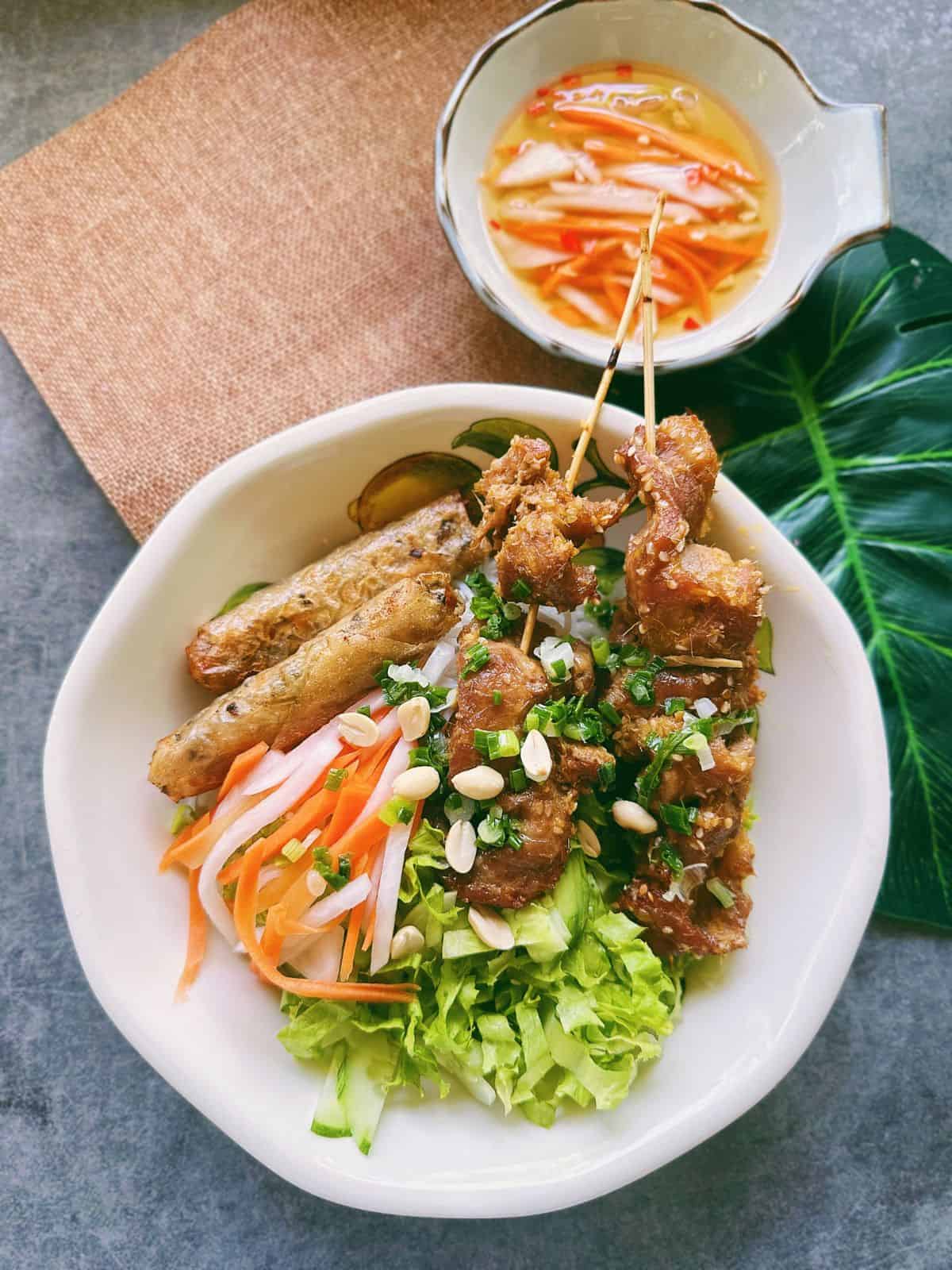 Bún Thịt Nướng with crispy egg rolls, fresh herbs, and a side of Nước Chấm topped with pickled carrots and daikon
