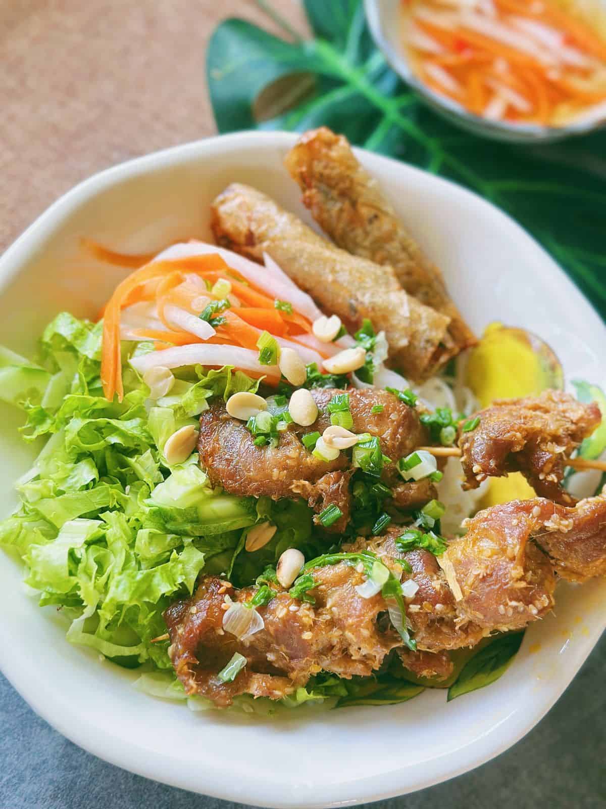 Vietnamese grilled pork noodle bowl served with chả giò, herbs, and dipping fish sauce with Đồ Chua garnish