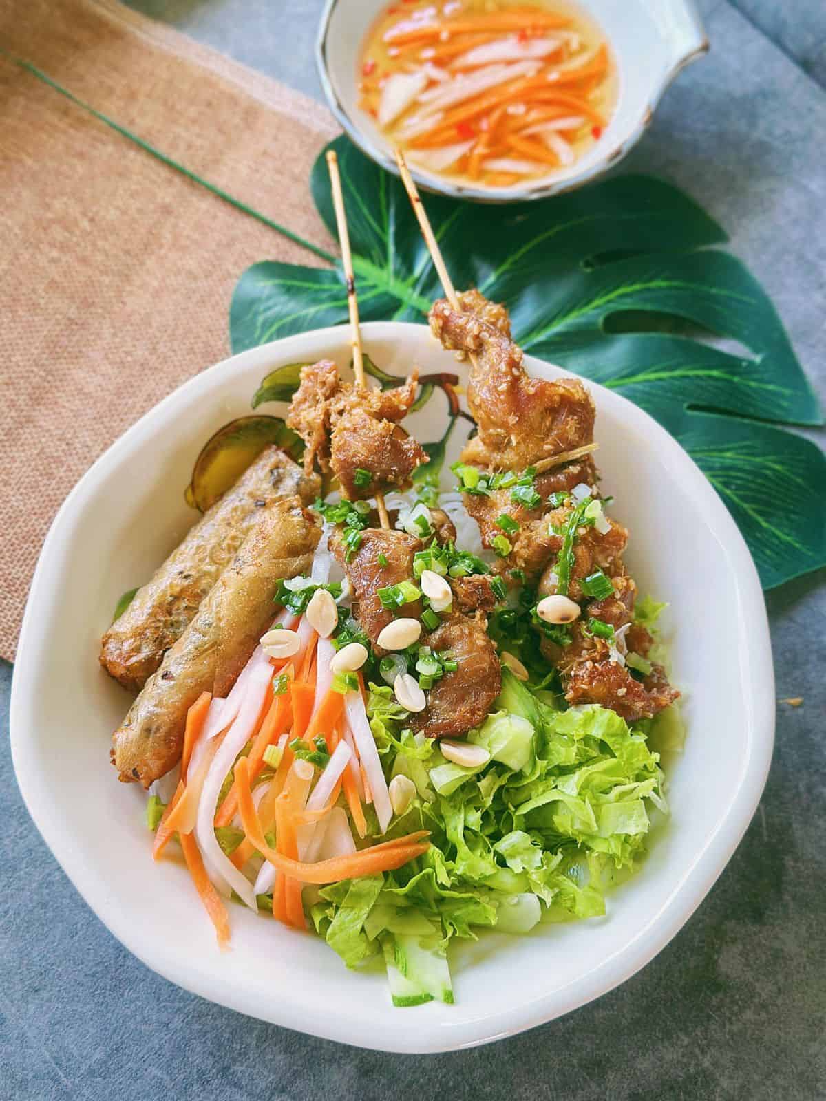 Bowl of Bún Thịt Nướng Chả Giò alongside Nước Chấm with pickled carrots and daikon.
