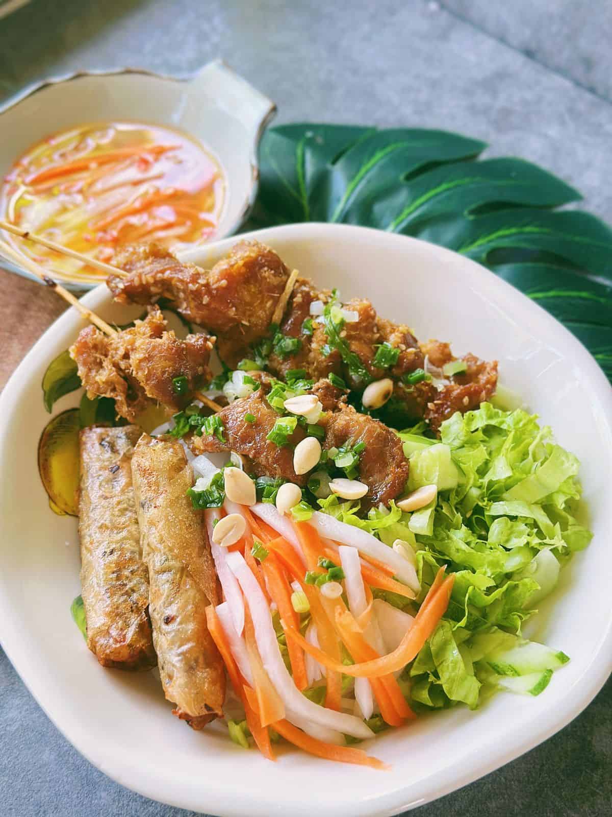 Bún Thịt Nướng with crispy egg rolls, fresh herbs, and a side of Nước Chấm topped with pickled carrots and daikon.