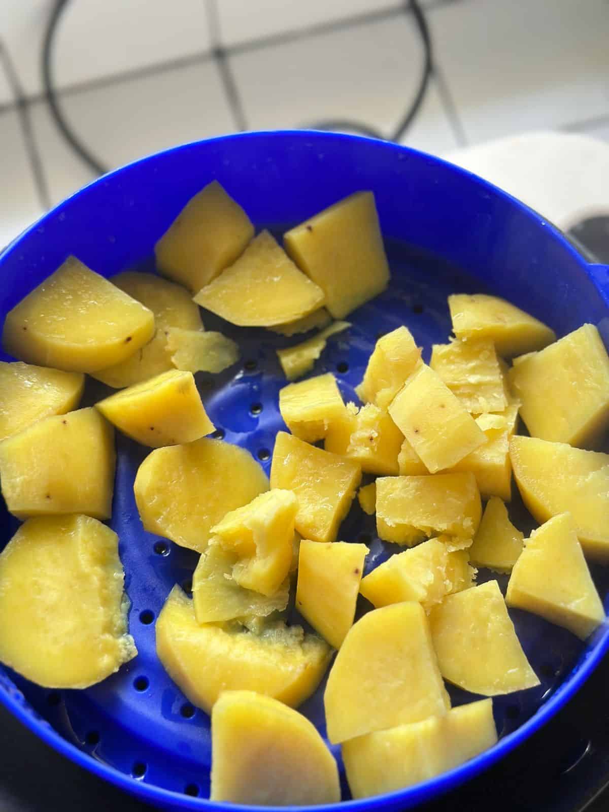 Chunks of boiled yellow yam placed in a steamer basket.