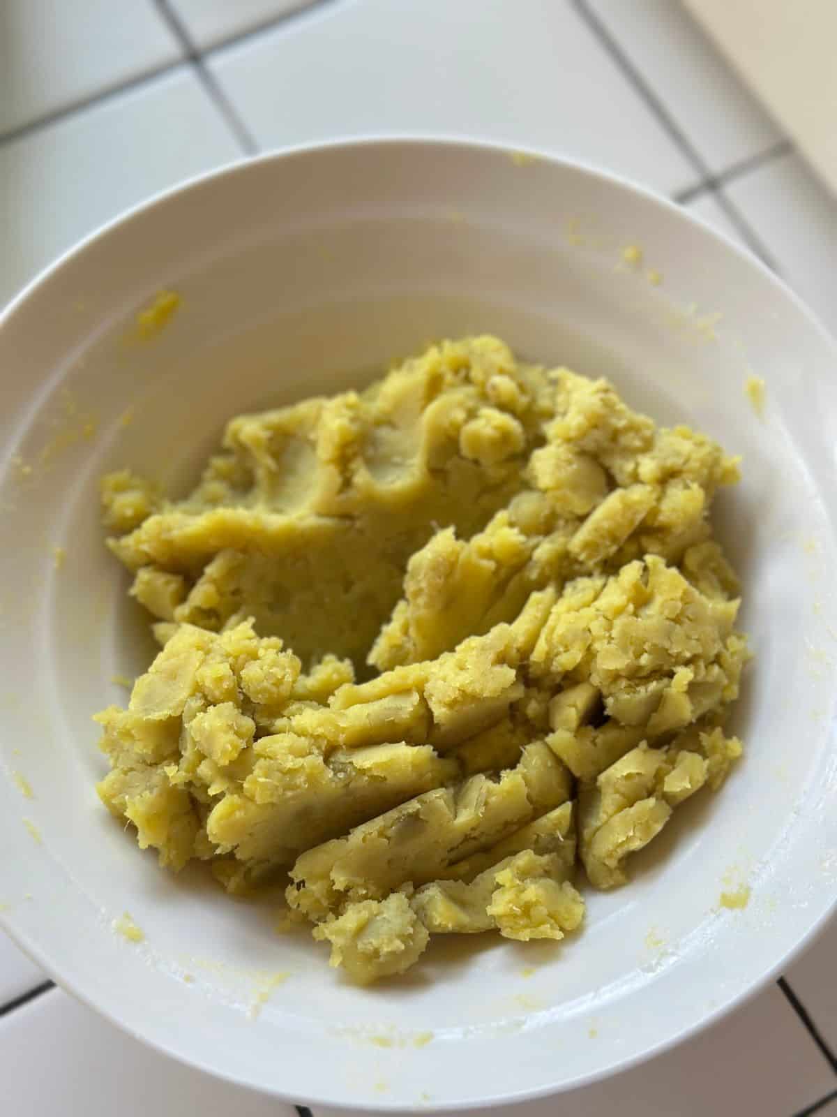 Mashed yellow yam in a white bowl, with a slightly crumbly texture.