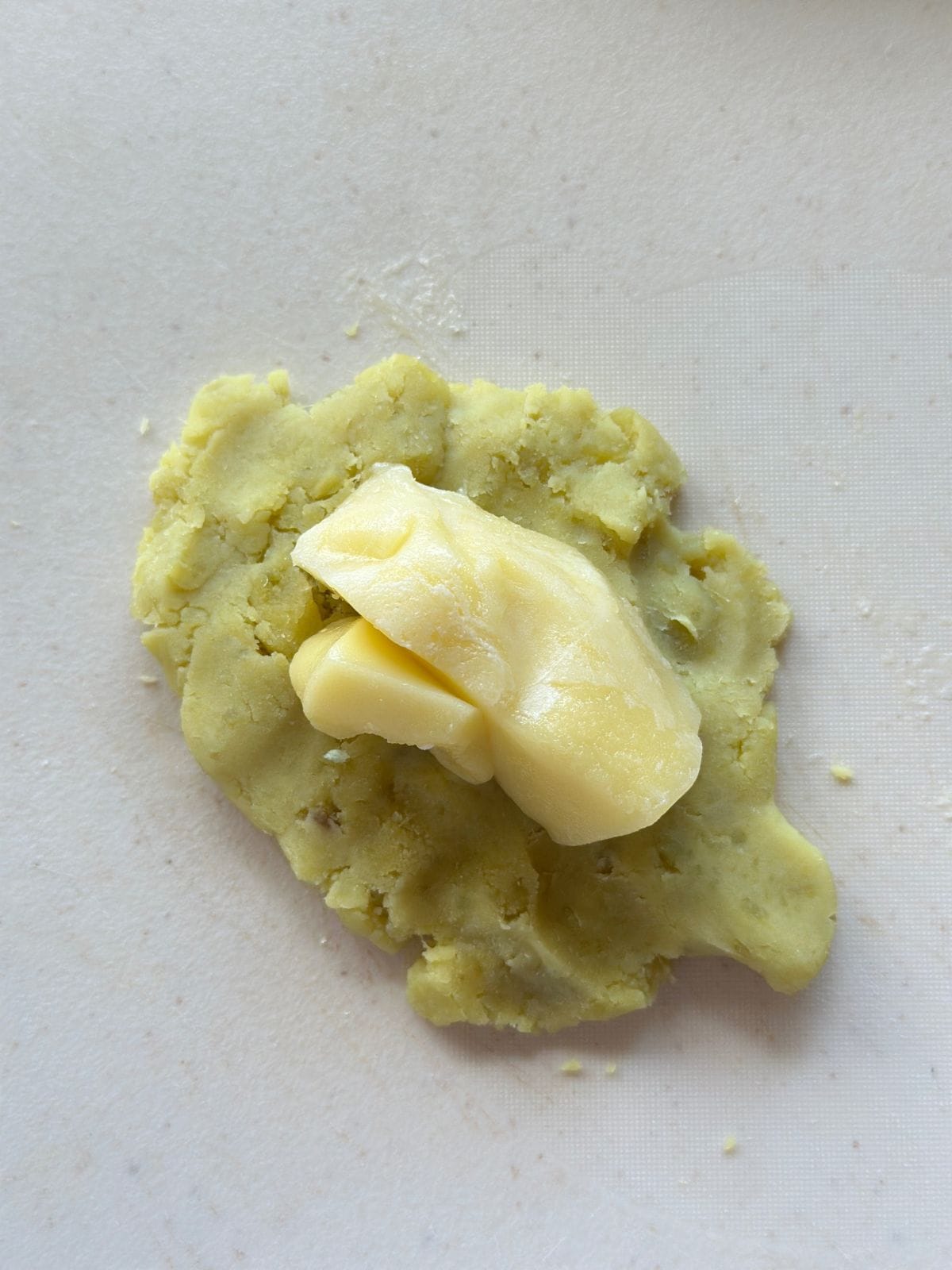 A flattened portion of yam dough with a piece of mozzarella cheese placed in the center.