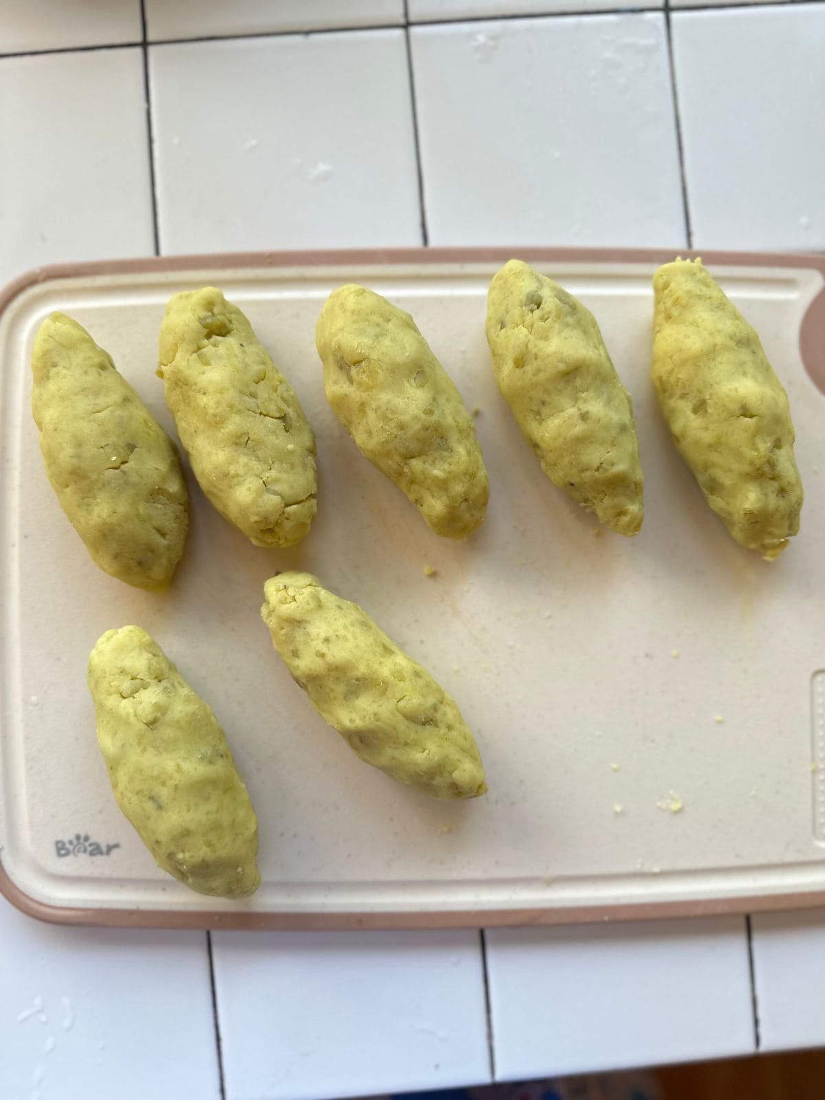 Seven oblong portions of sweet potato dough shaped into small rolls on a cutting board.