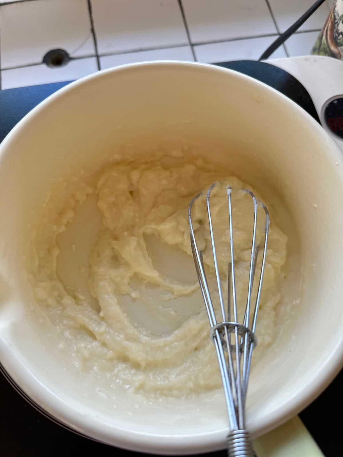 A white bowl containing a smooth, creamy batter being whisked with a metal whisk.