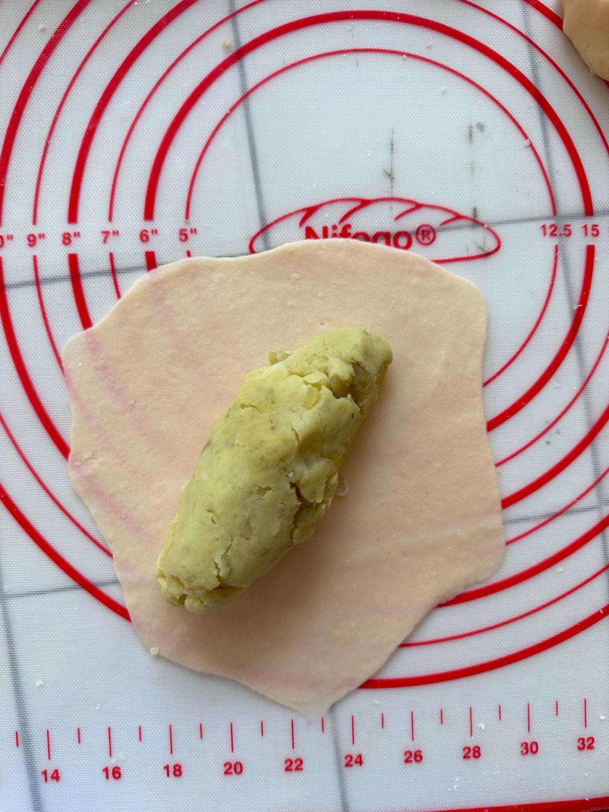 A flattened piece of dough on a pastry mat with a portion of yam filling placed in the center.