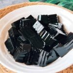 Close-up of glossy black grass jelly cubes served in a white bowl.