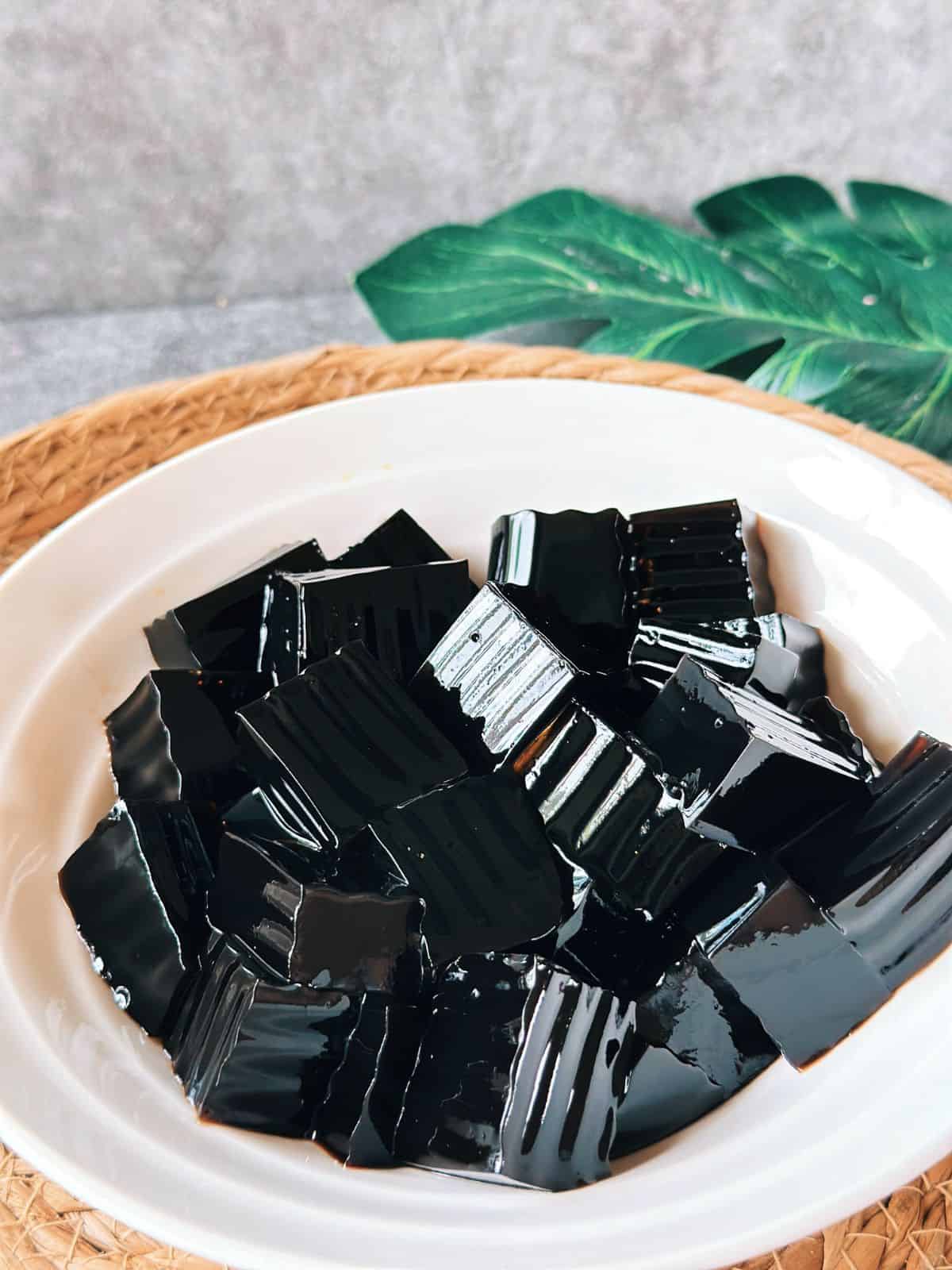 Close-up of glossy black grass jelly cubes served in a white bowl.