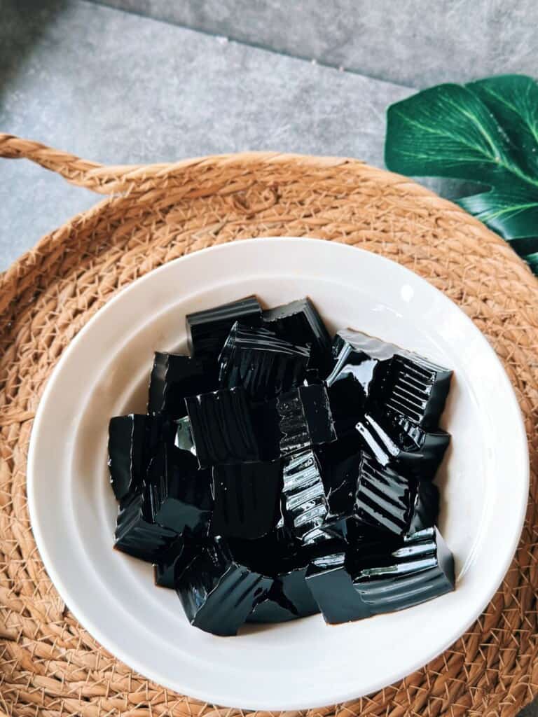 Chilled grass jelly cut into shiny cubes, sitting in a plain white bowl.