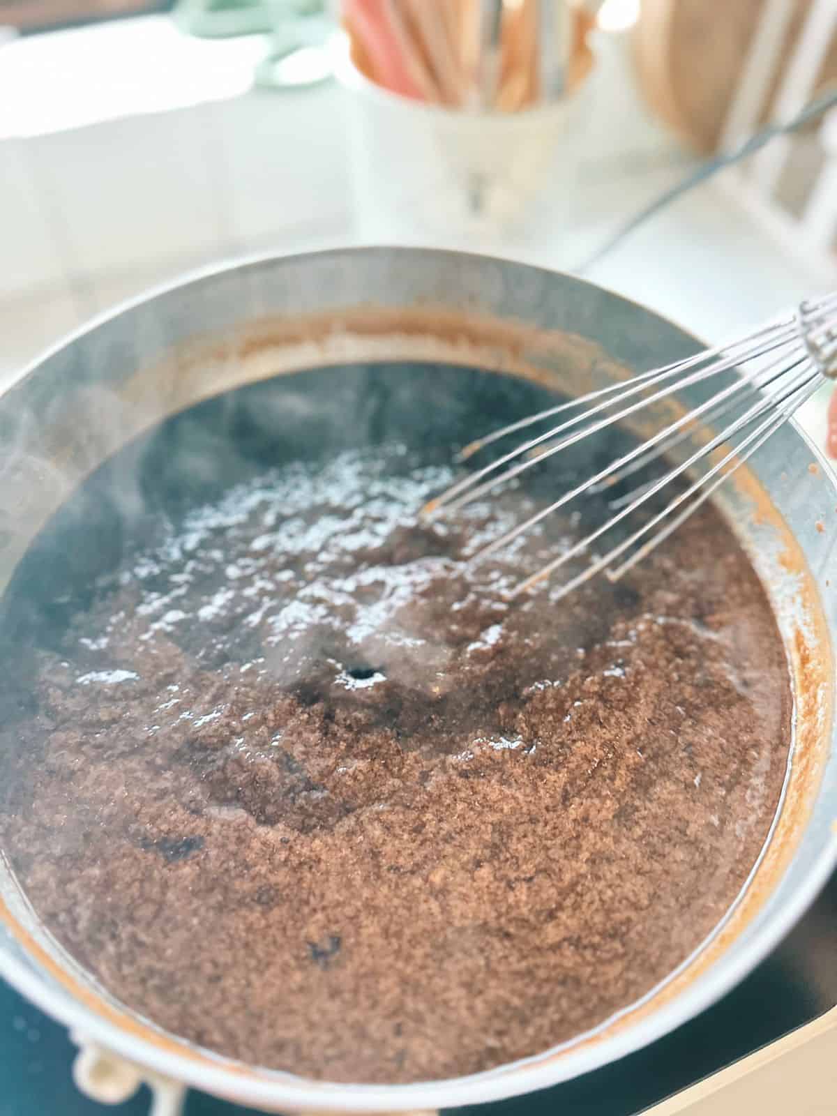 Grass jelly mixture in a pot starting to thicken and look lumpy while cooking.