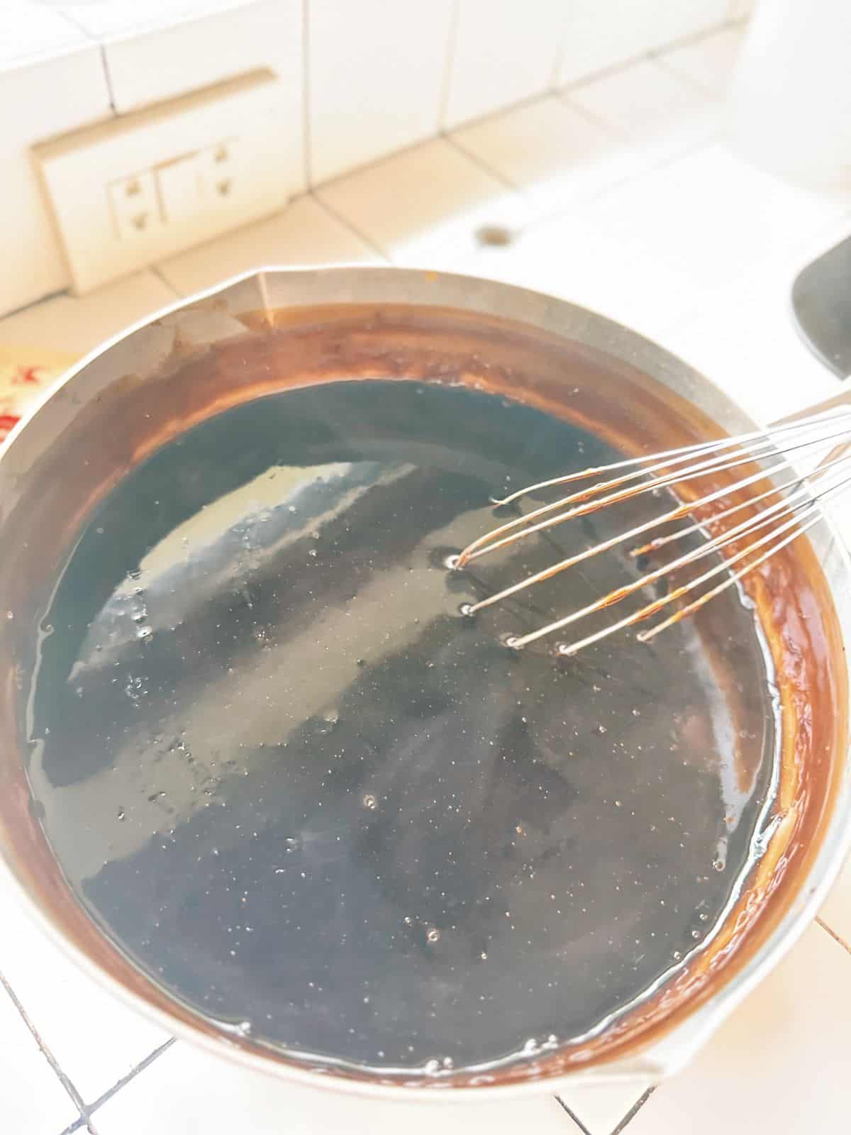 Cooked grass jelly mixture in a pot, smooth and silky after constant whisking.