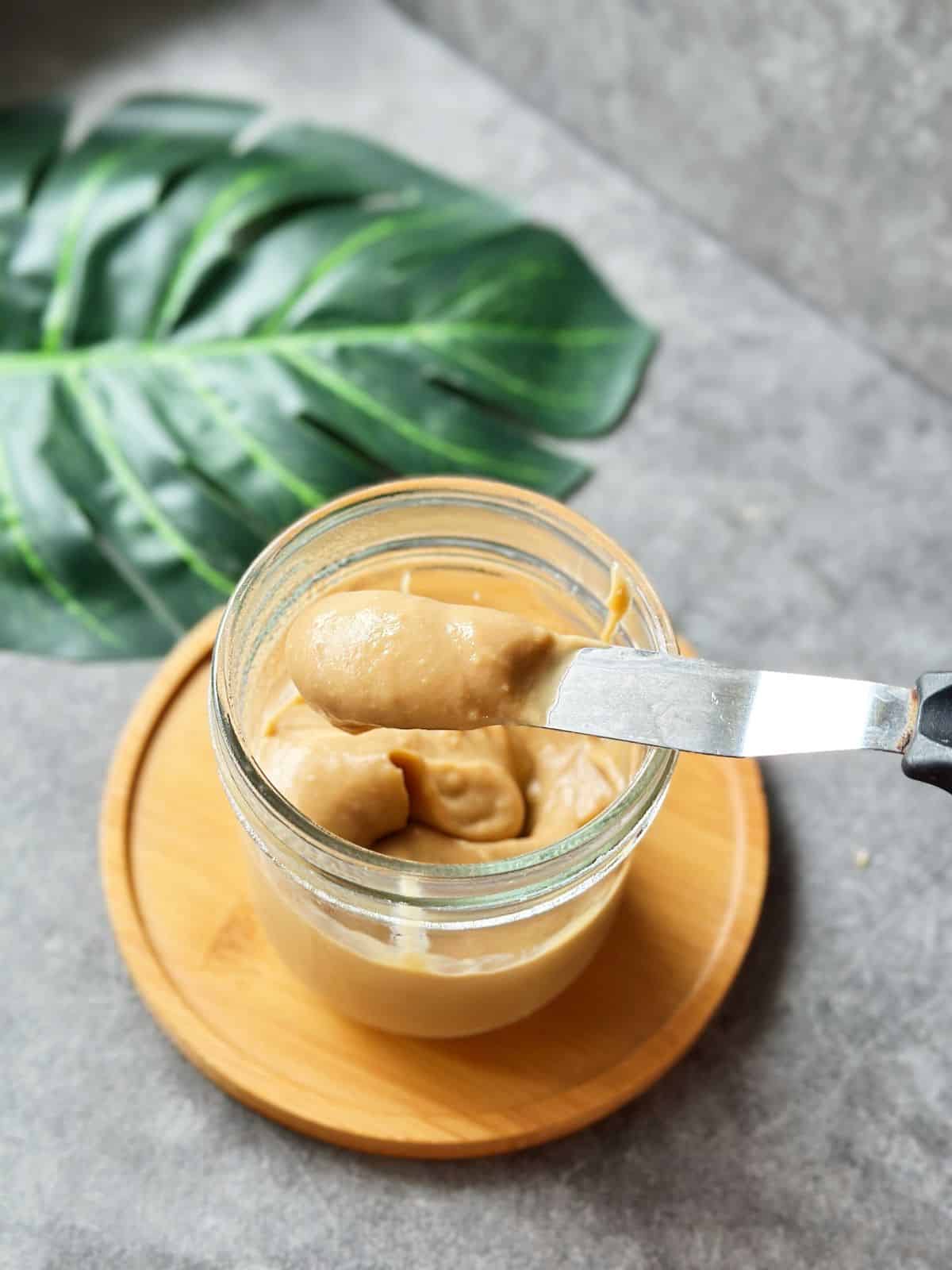 Close-up of Hainanese Kaya coconut jam in a glass jar, with a knife dipped into the thick, caramel-like spread.
