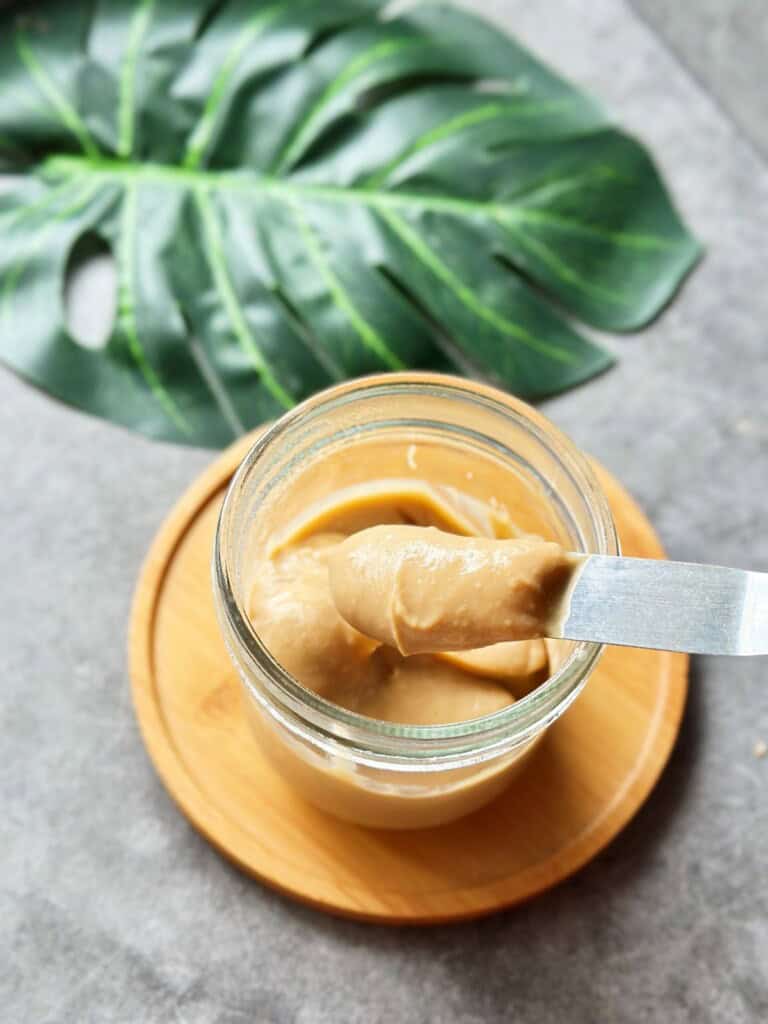 Close-up of Hainanese Kaya coconut jam in a glass jar, with a knife dipped into the thick, caramel-like spread.